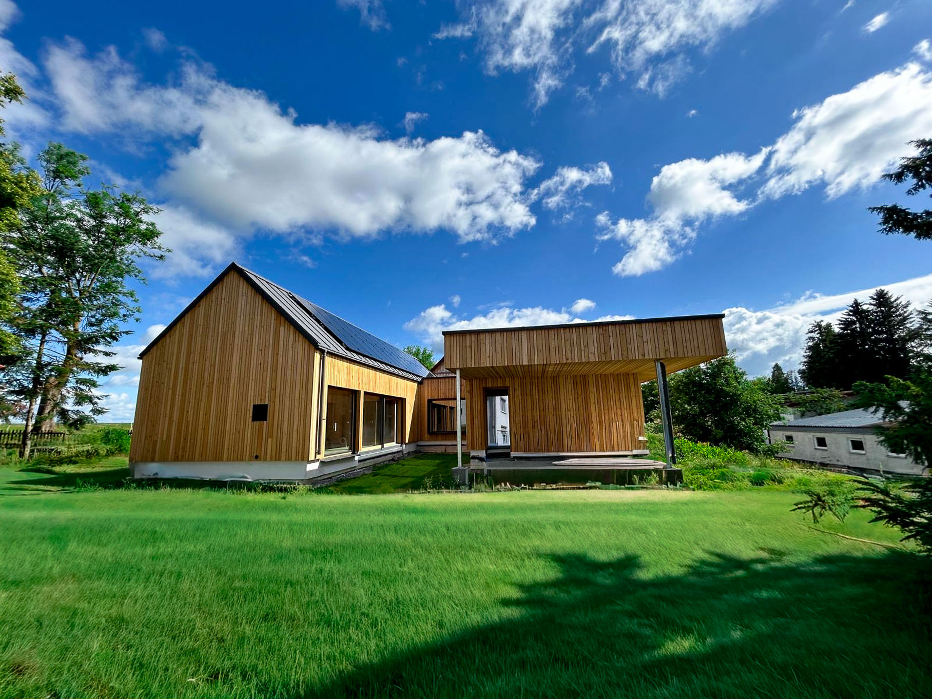 Modernes Haus mit naturbelassener Holzfassade, anthrazitfarbenem Metalldach & großzügigen Fensterflächen.