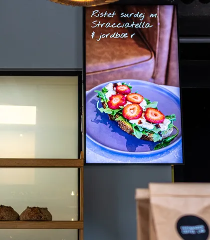 Digital menu screen showing toasted sourdough topped with stracciatella cheese, sliced strawberries, and greens on a blue plate.