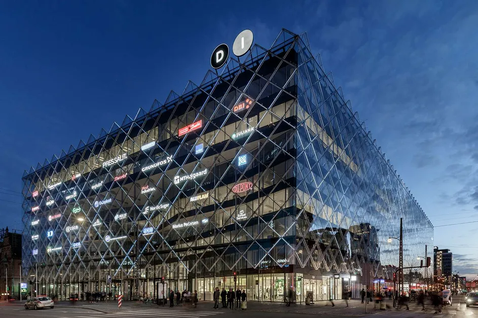 Modern office building with glass facade covered in illuminated company logos during twilight.