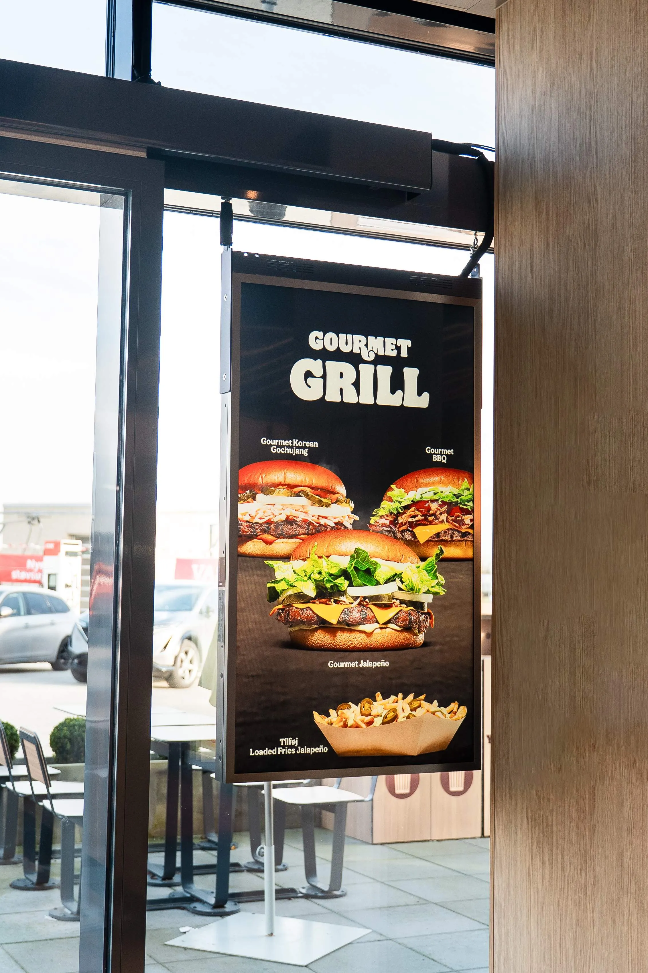 Menu board displaying three burgers named Gourmet Korean Gochujang, Gourmet BBQ, Gourmet Jalapeño, and a serving of loaded fries with jalapeños.