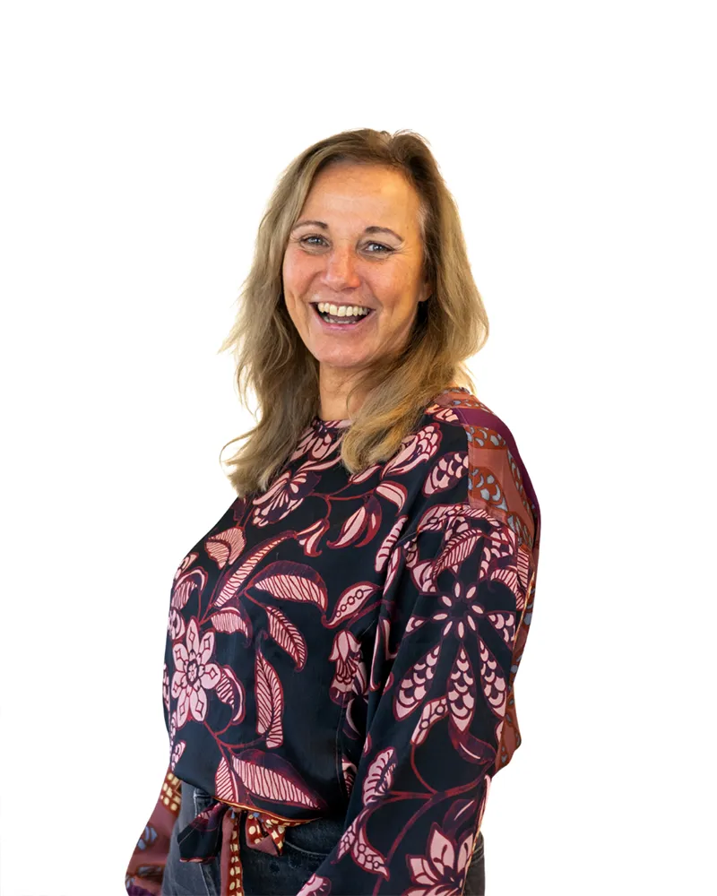 Vrouw met blond haar die lacht, gekleed in een zwarte blouse met paarsrode bloemenprint.