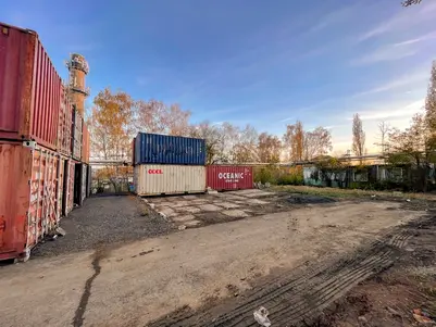 Průmyslové nádvoří s několika naloženými přepravními kontejnery a podzimními stromy na pozadí za jasné oblohy.