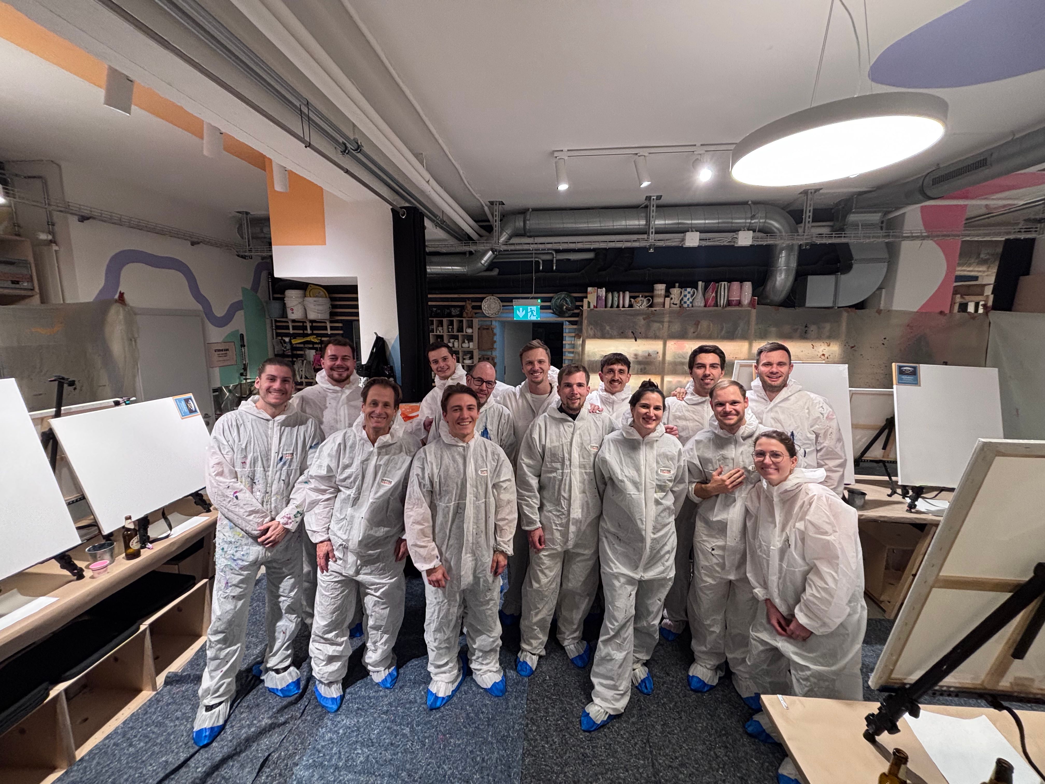 Group of people in white protective coveralls and blue shoe covers standing in an art studio with blank canvases.