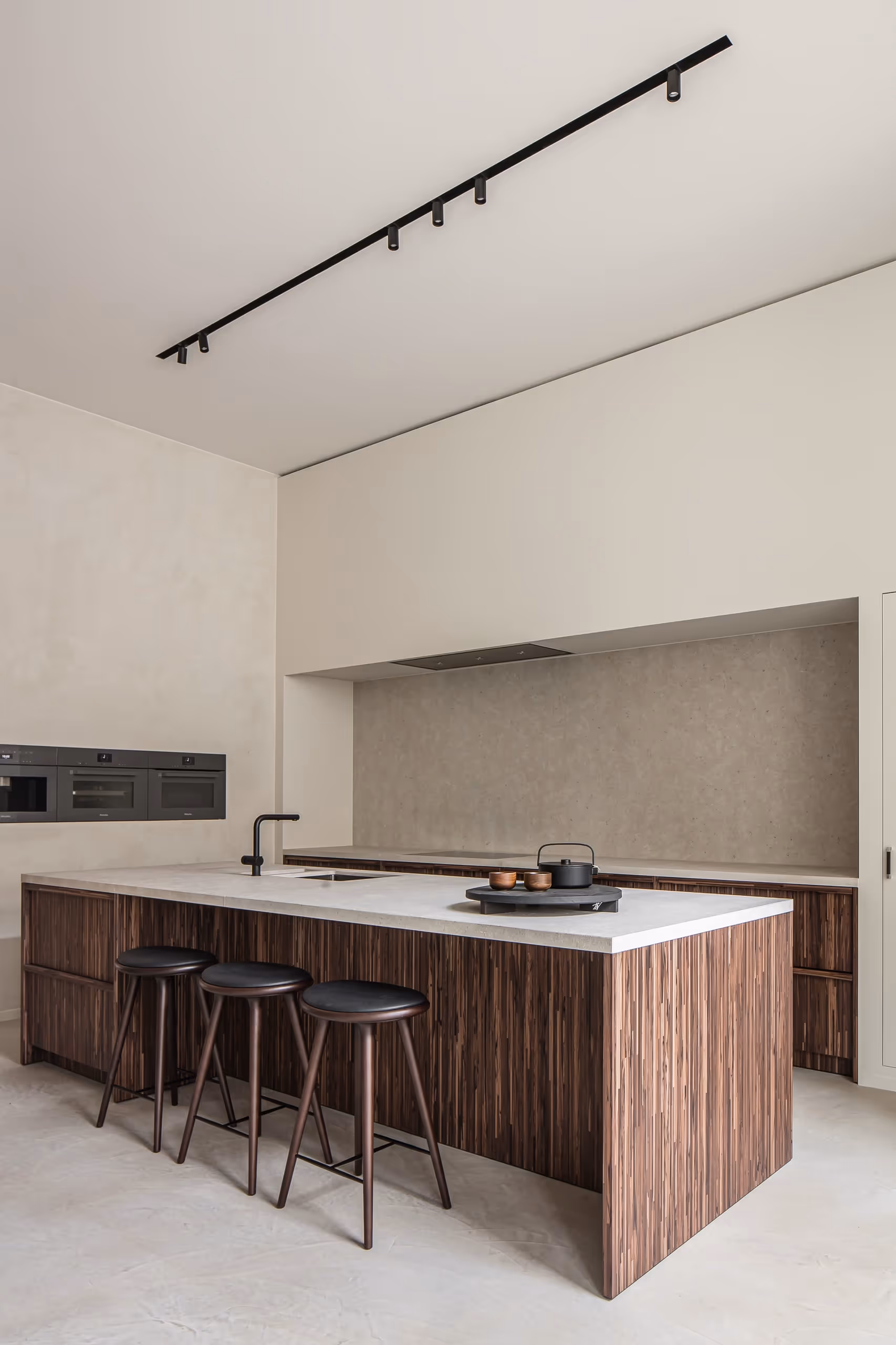 Moderne keuken met een wit werkblad, donker houten keukeneiland, drie zwarte barkrukken en ingebouwde zwarte apparatuur.