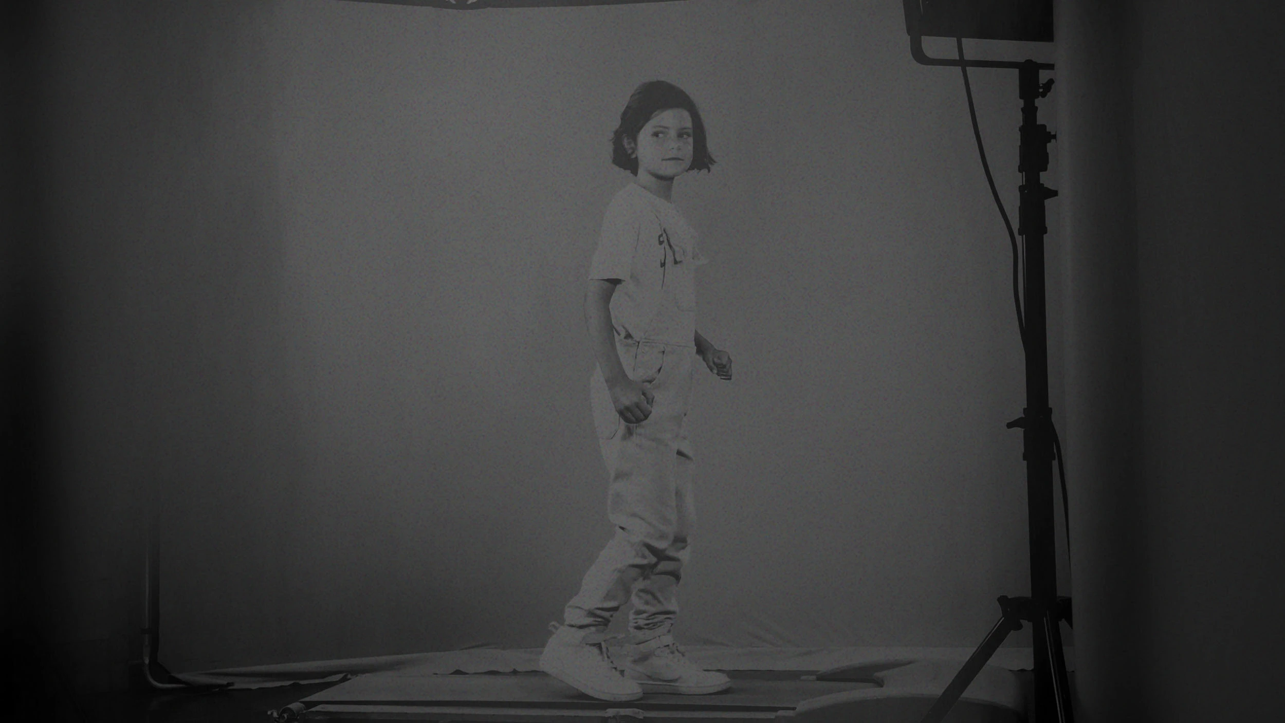 Young girl with short hair standing and looking to the side in a studio with lighting equipment. A still from a Fashion and Lifestyle video production.
