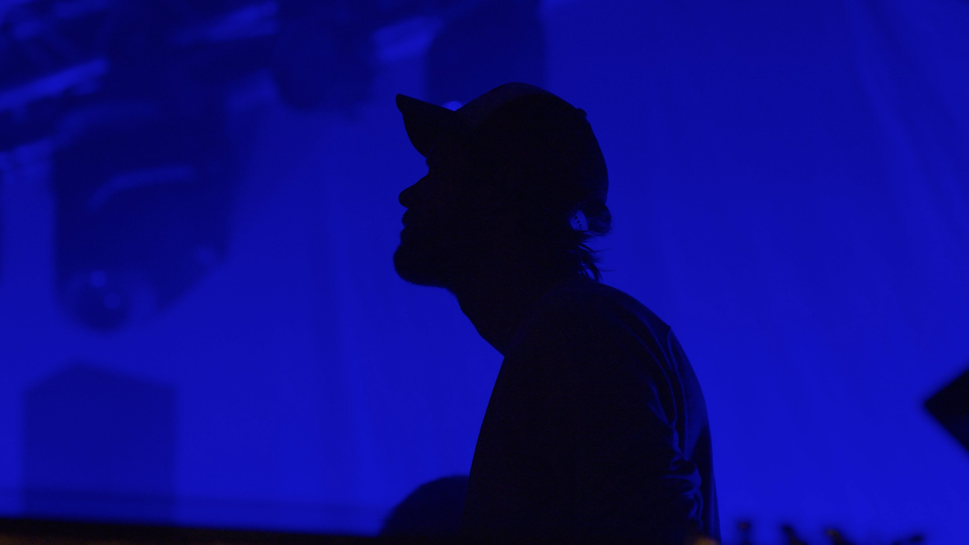 Silhouette of a man wearing a baseball cap against a deep blue background. A Video Still from a Video Production captured at Tomorrowland Belgium for the Aftermovie.