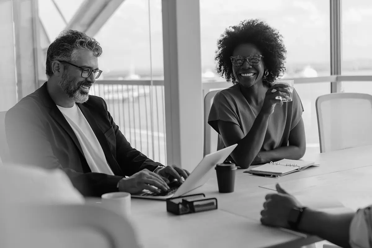 Two colleagues smiling and having a conversation during a meeting in a bright office.