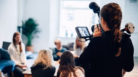 Camerawoman filming a group discussion in an office