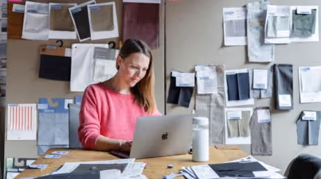 Woman working on laptop with fabric samples pinned to wall