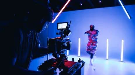 Camera operator filming dancer in neon-lit studio