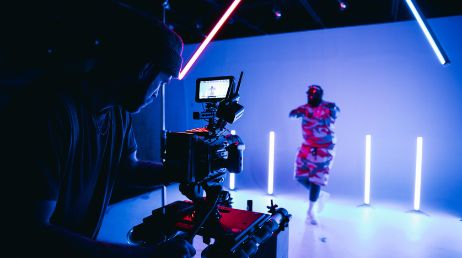 Camera operator filming dancer in neon-lit studio