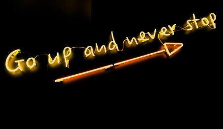 Neon sign saying 'Go up and never stop' with arrow