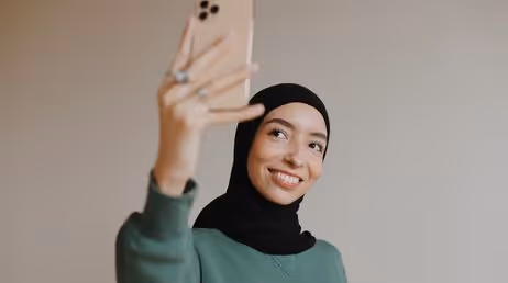 Smiling woman in hijab taking selfie with iPhone
