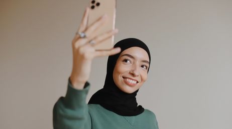 Smiling woman in hijab taking selfie with iPhone
