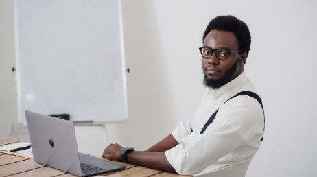 Man with glasses sitting at a desk with a laptop