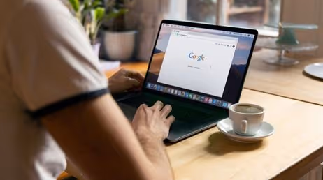 Person using Google search on a laptop with coffee nearby