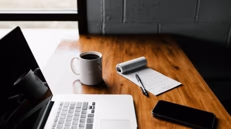 Laptop with tea cup along with note taking paper and smartphone on desk