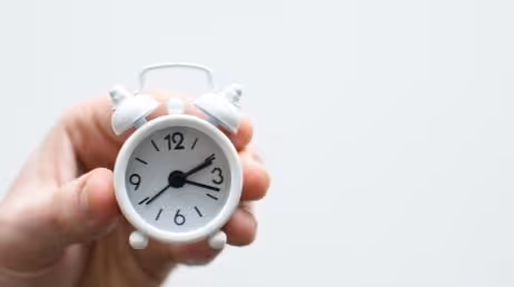 holding a small white alarm clock