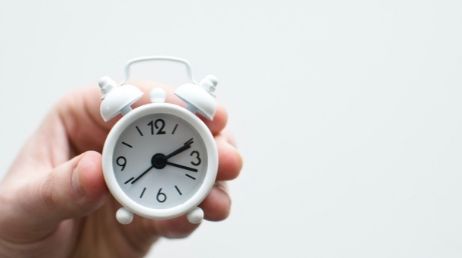 holding a small white alarm clock