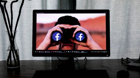 Person looking through Facebook-themed binoculars on monitor