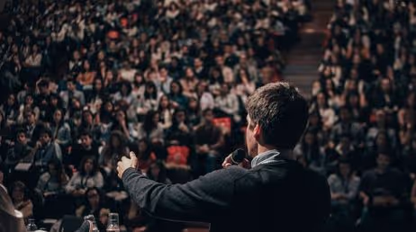 Speaker addressing a large audience at a conference event"