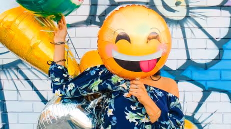 Woman holding emoji balloon covering her face