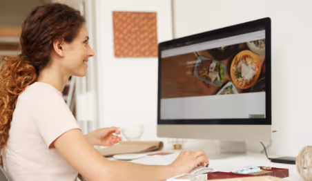 "Woman browsing a food website on desktop while drinking coffee