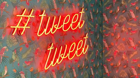 Neon hashtag tweet sign on a tropical themed background