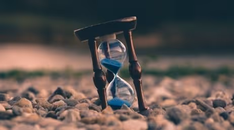 Hourglass with blue sand on rocky ground at sunset
