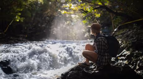 Person sitting by a waterfall in the forest