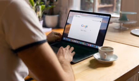 Person using Google search on laptop with coffee