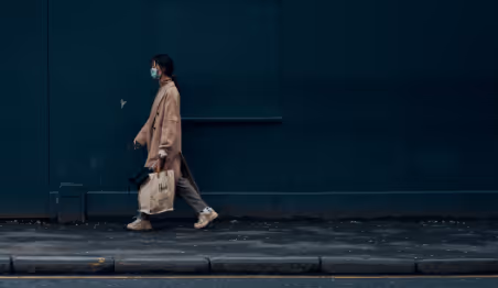 Person walking outside wearing a mask and carrying a bag