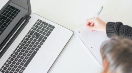 Person taking notes while working on laptop