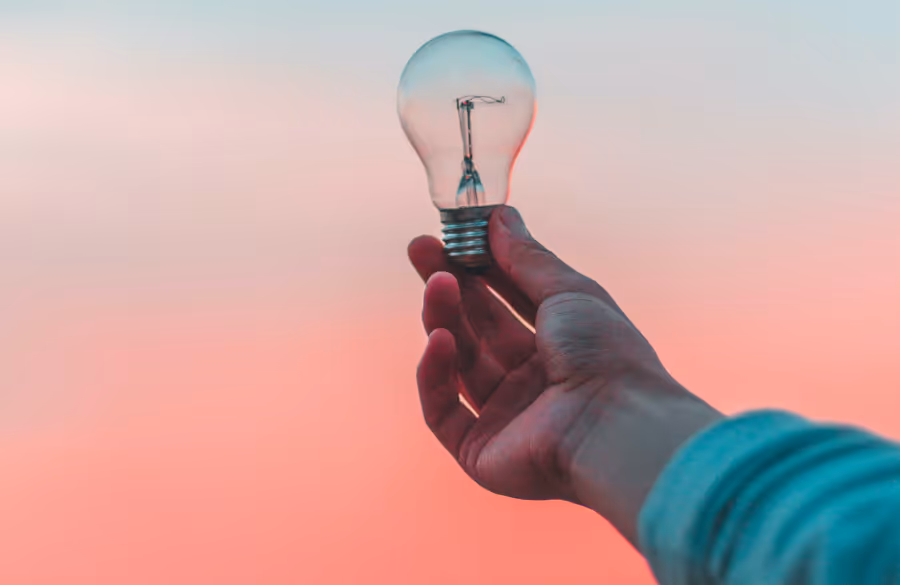 Person holding a lightbulb against colorful sky
