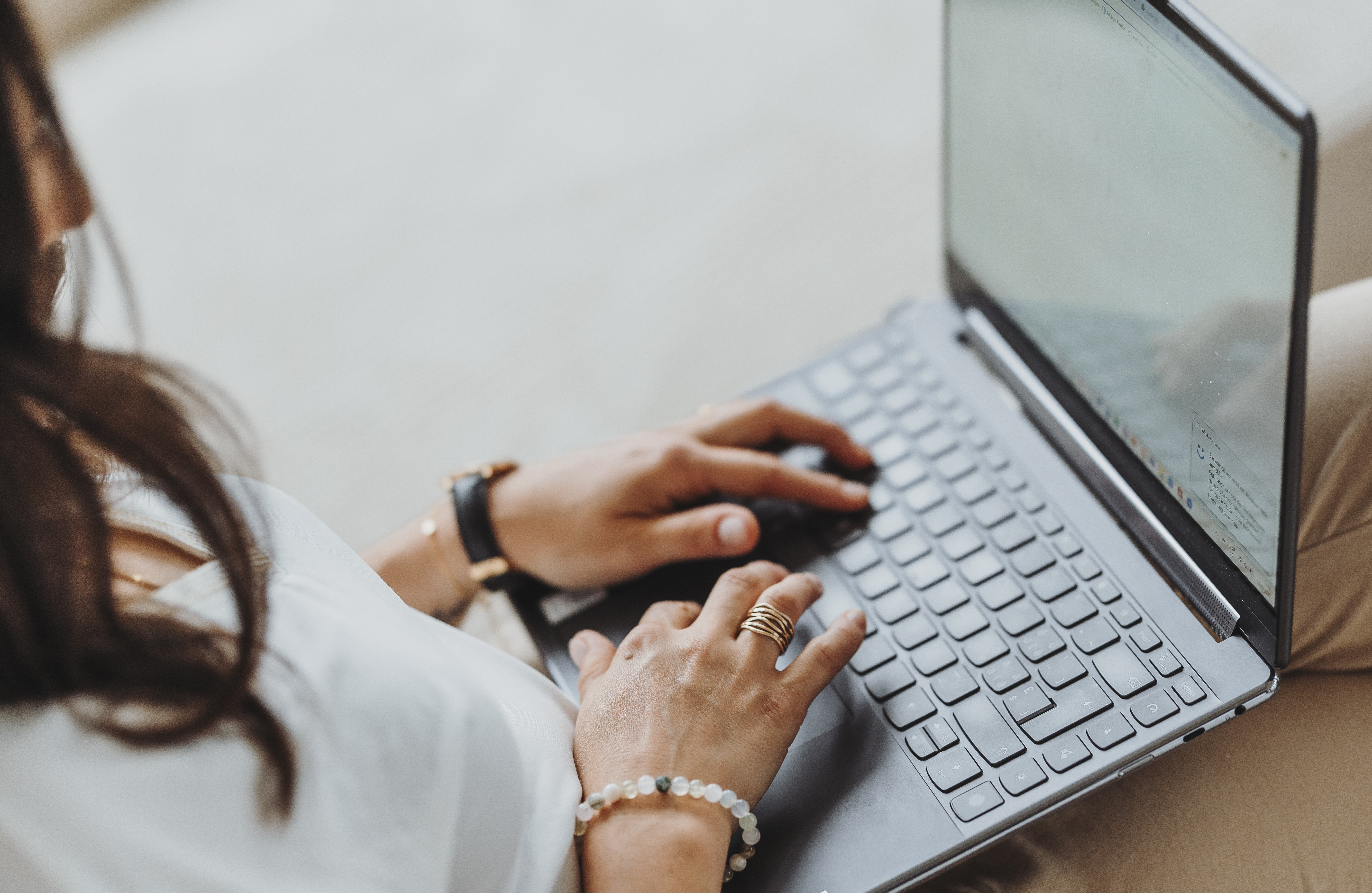 Frau tippt auf der Tastatur eines aufgeklappten Laptops auf ihrem Schoß.