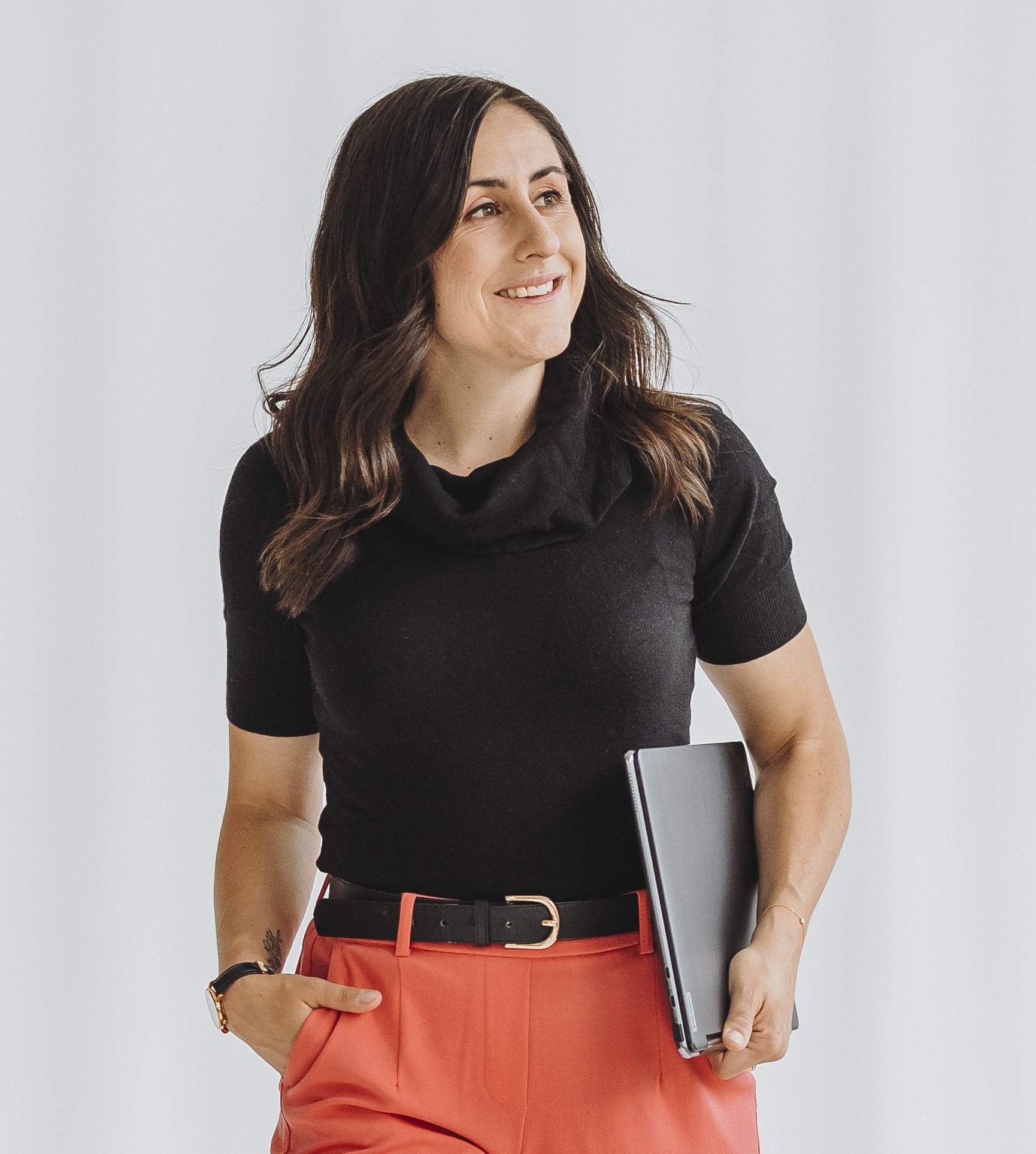 Sandra Wettstein mit schwarzem Oberteil und roten Hosen hält einen Laptop und lächelt zur Seite.