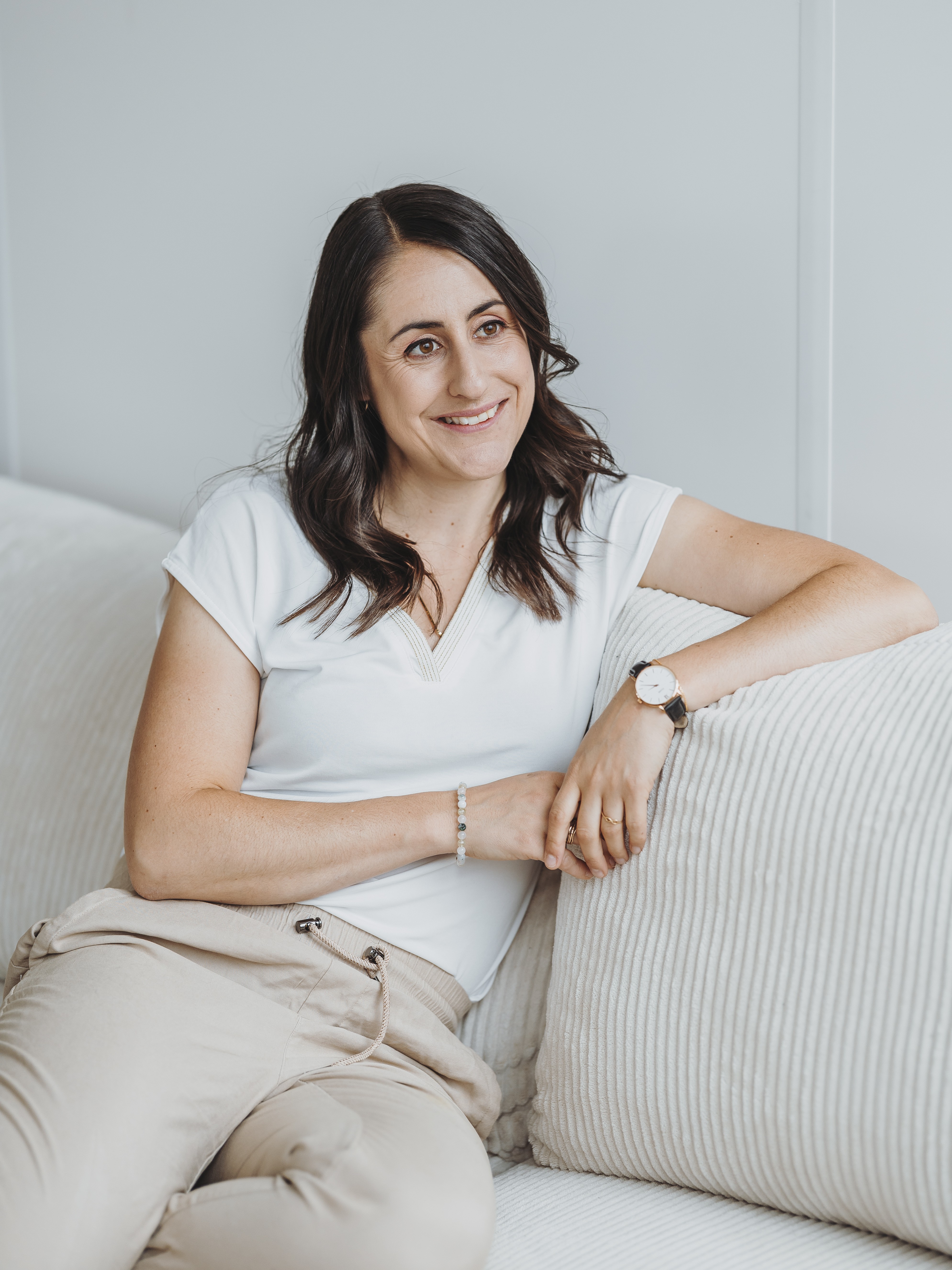 Sandra Wettstein mit dunklen, gewellten Haaren sitzt entspannt auf einem beigen Sofa und lächelt.