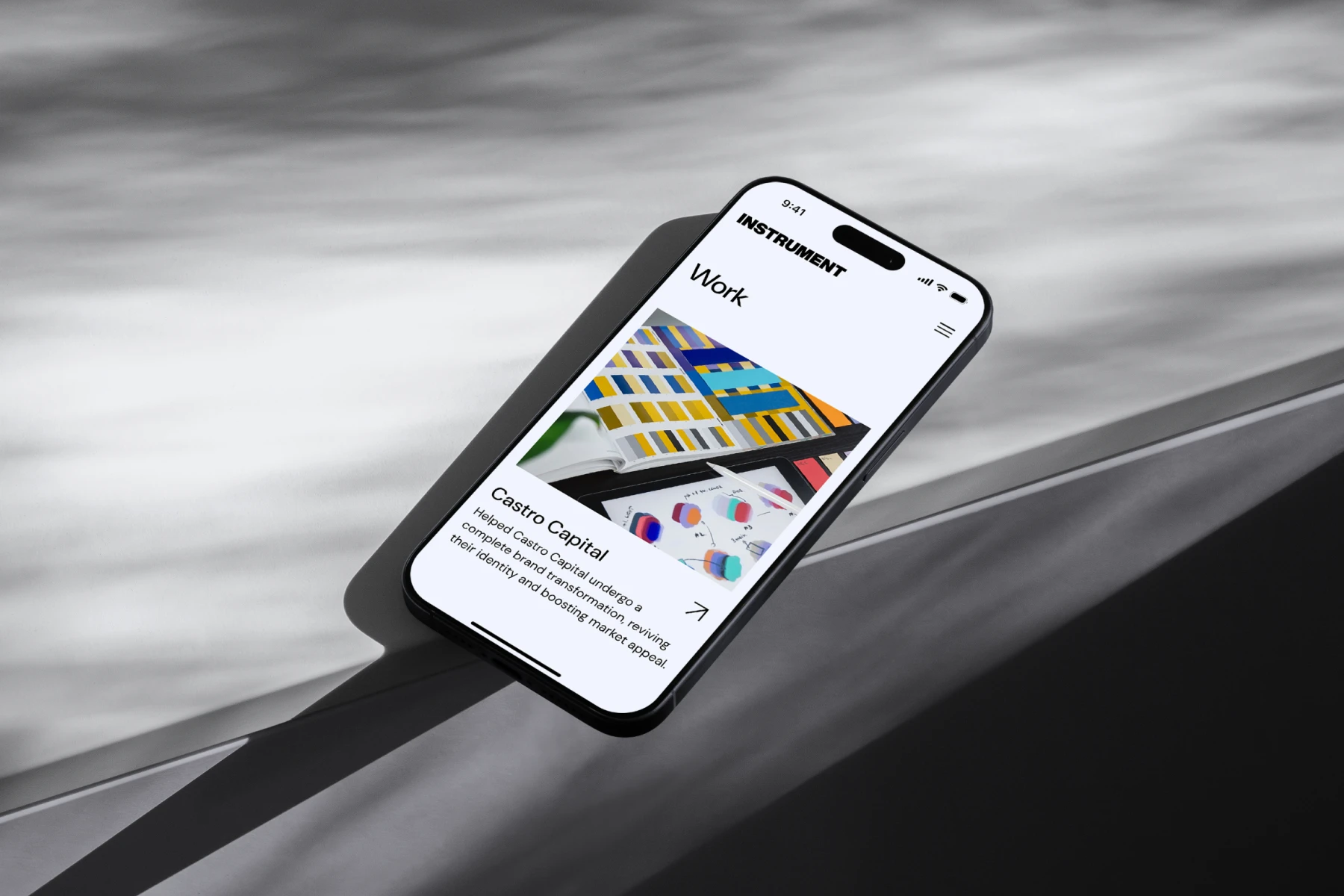 Smartphone on a gray surface displaying a webpage titled 'Work' featuring a project called Castro Capital with colorful design elements and diagrams.