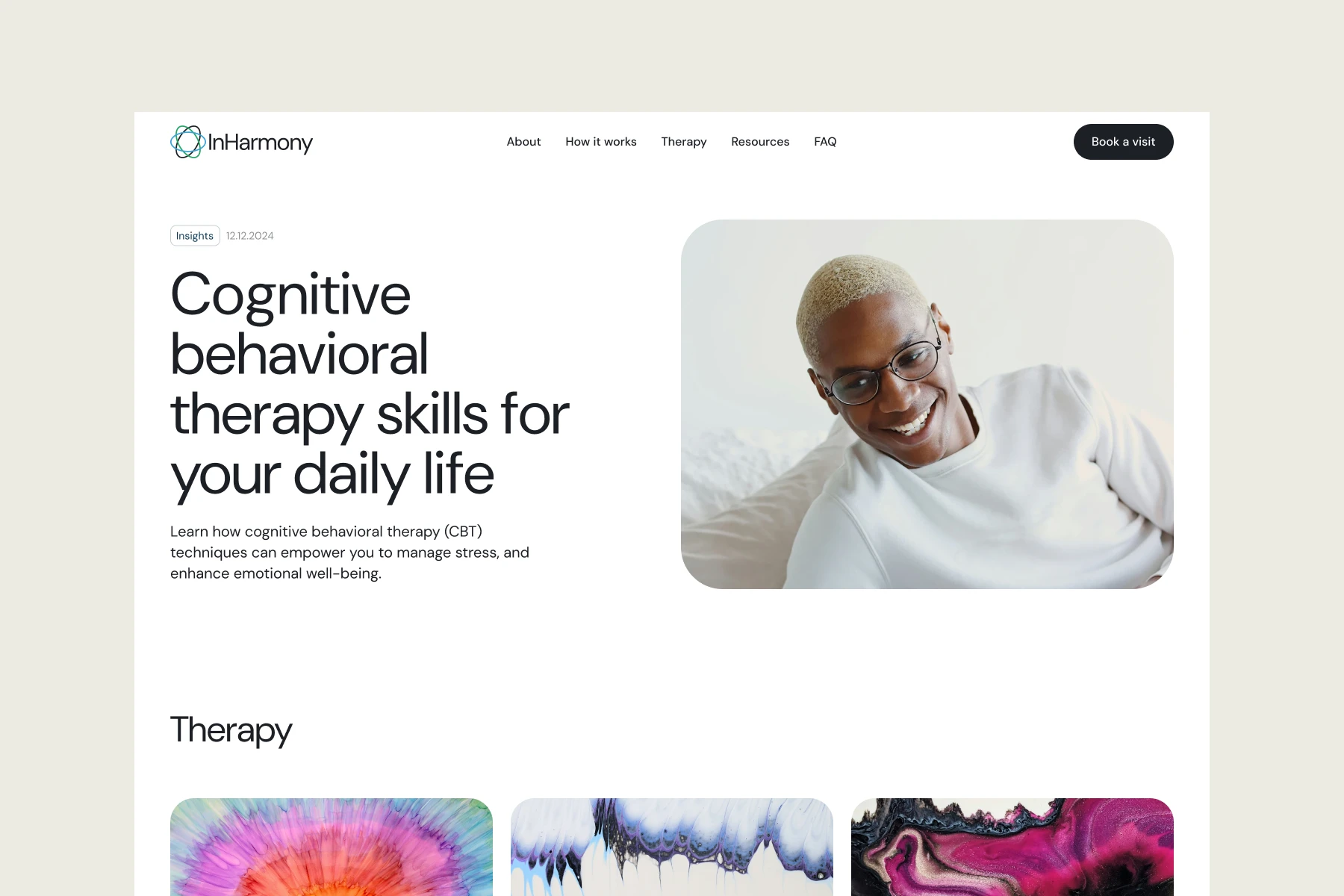 Smiling person with short blonde hair and glasses reclining on a bed wearing a white sweater.