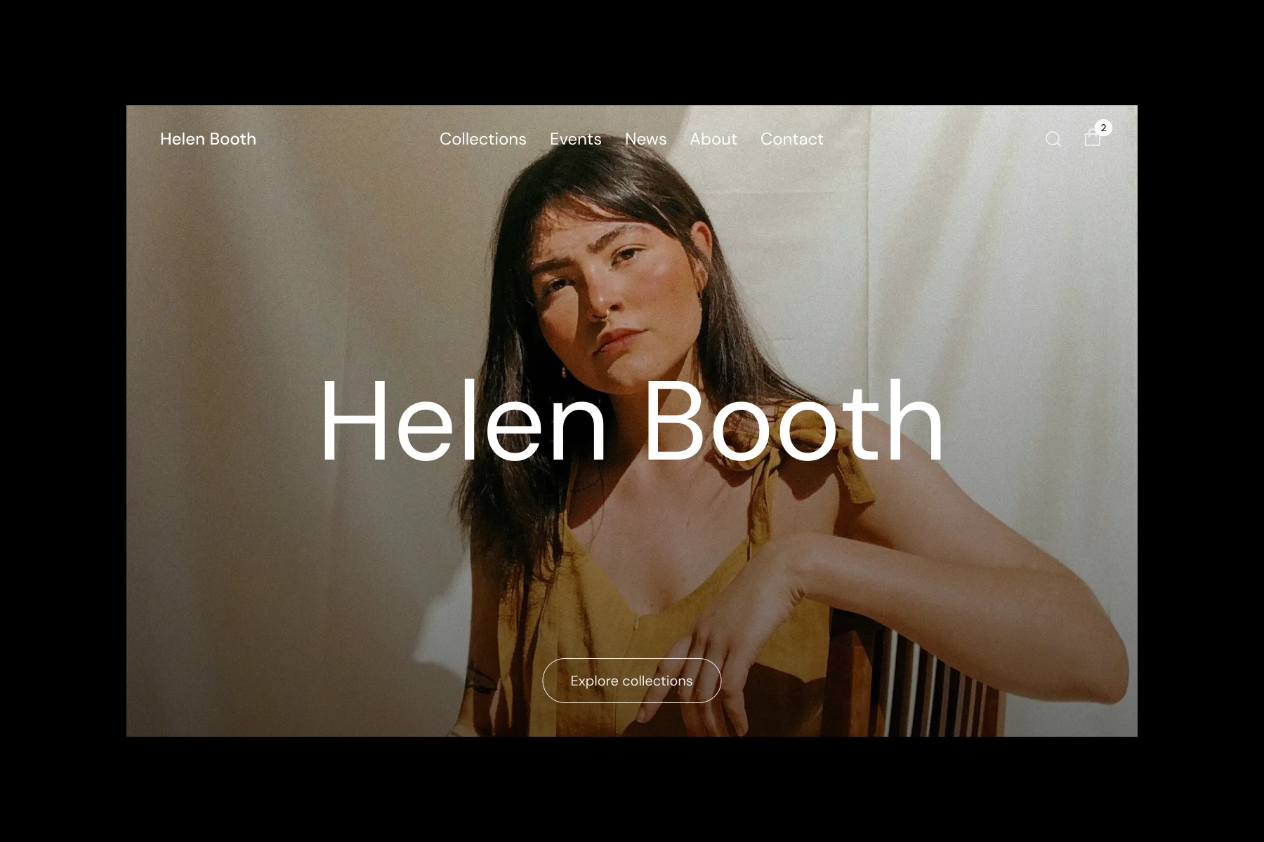 Young woman with long dark hair wearing a mustard sleeveless top, sitting with one arm resting on a chair back against a light beige background.