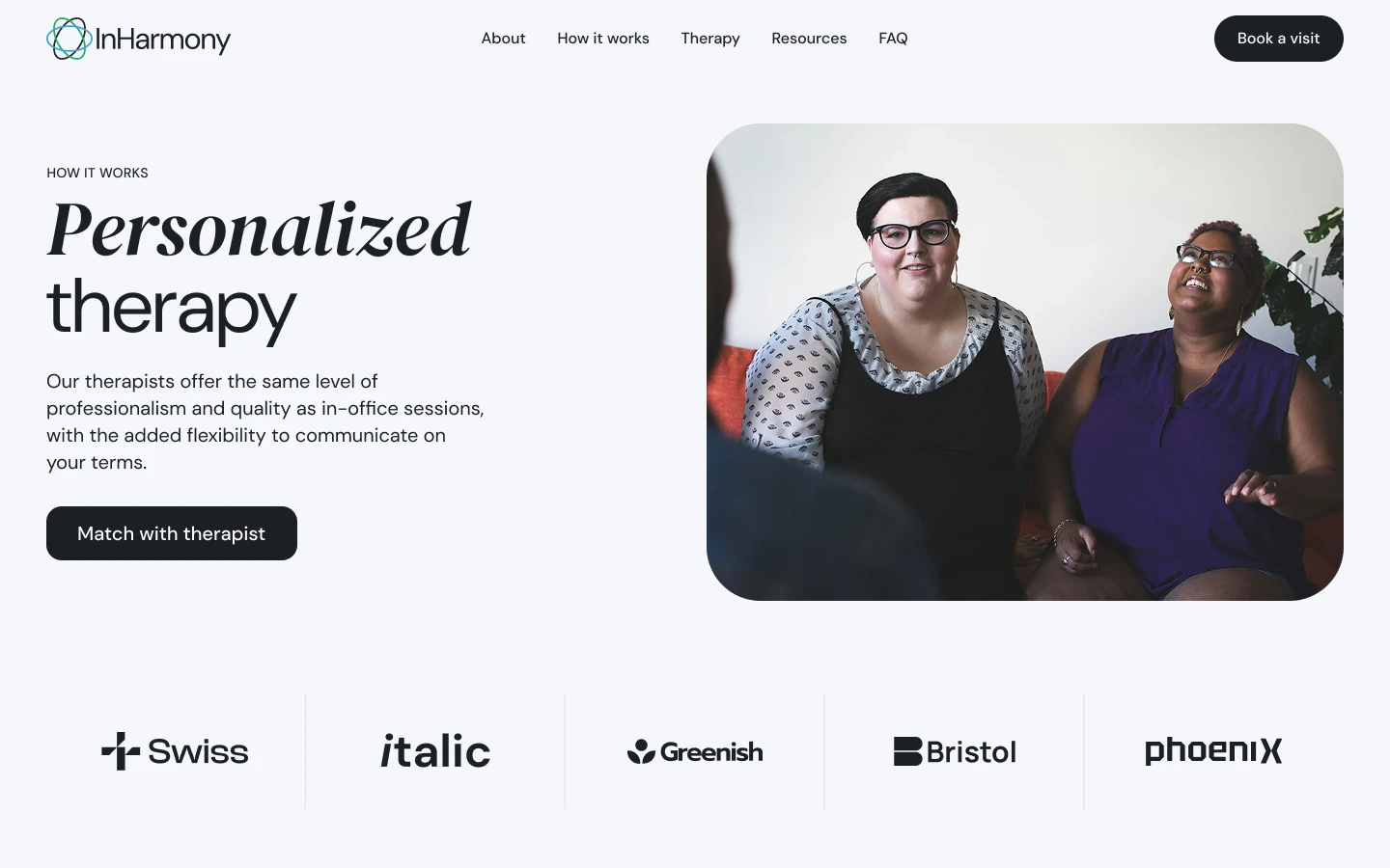 Two women sitting and smiling during a therapy session, one wearing glasses and a black dress with a patterned blouse, the other in a purple sleeveless top.