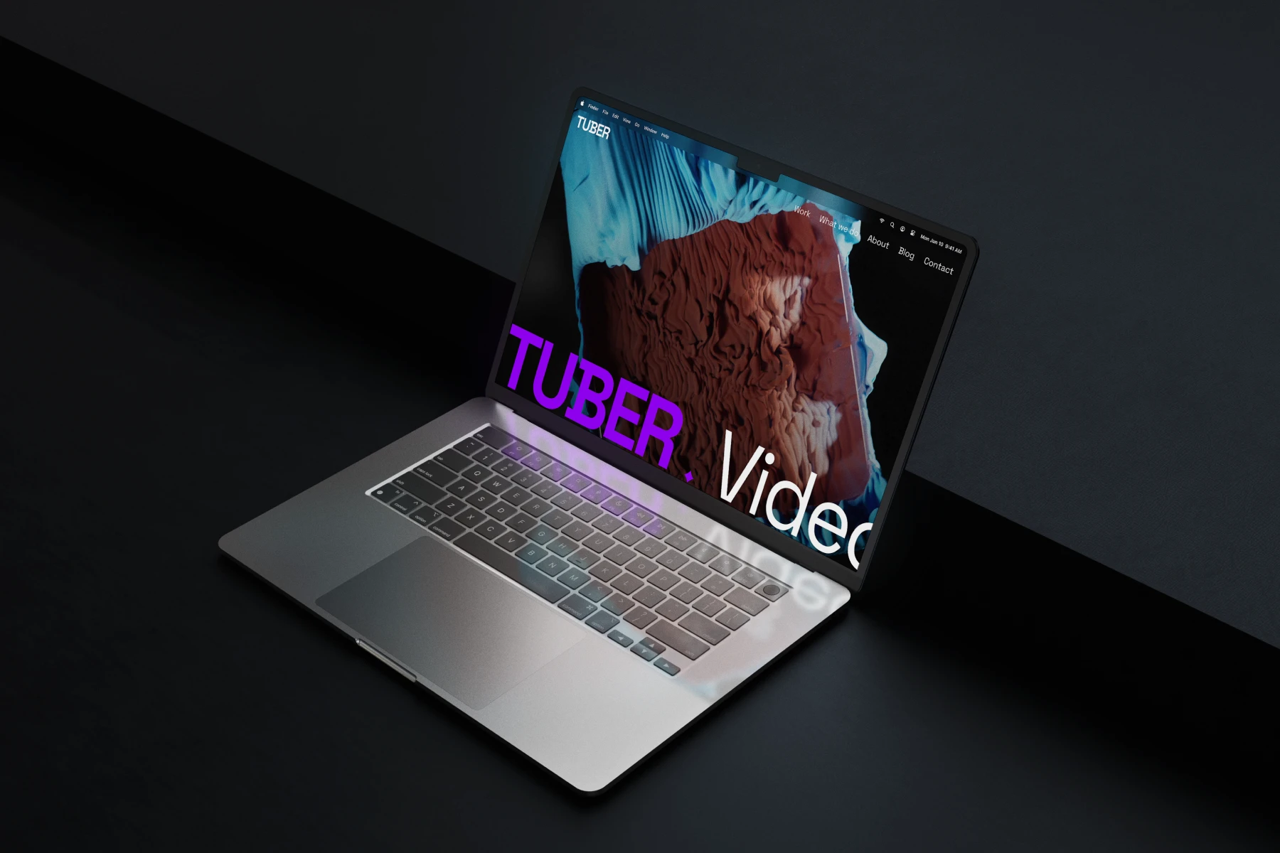 Open laptop on a dark surface showing a website with large purple text 'TUBER' and a reddish abstract image on the screen.