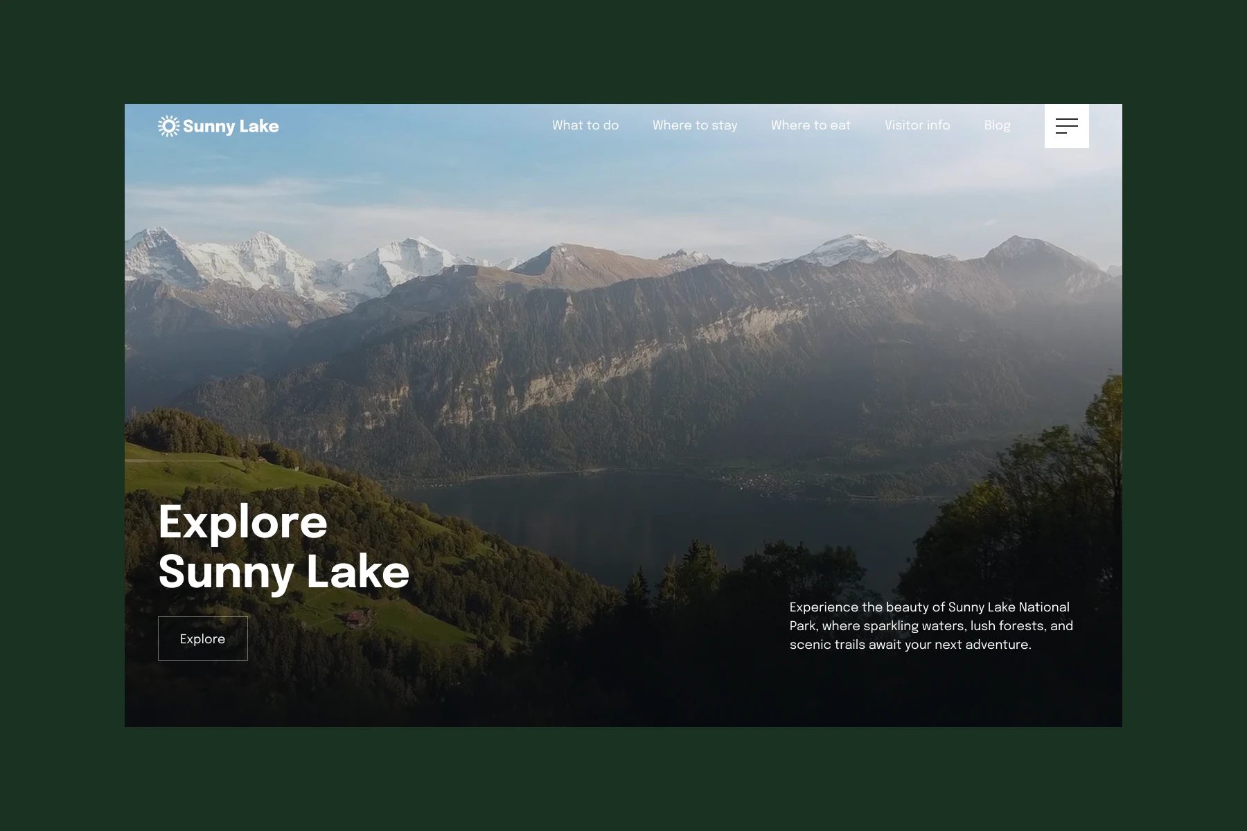 View of a lake surrounded by forested hills and snow-capped mountains under a clear sky.