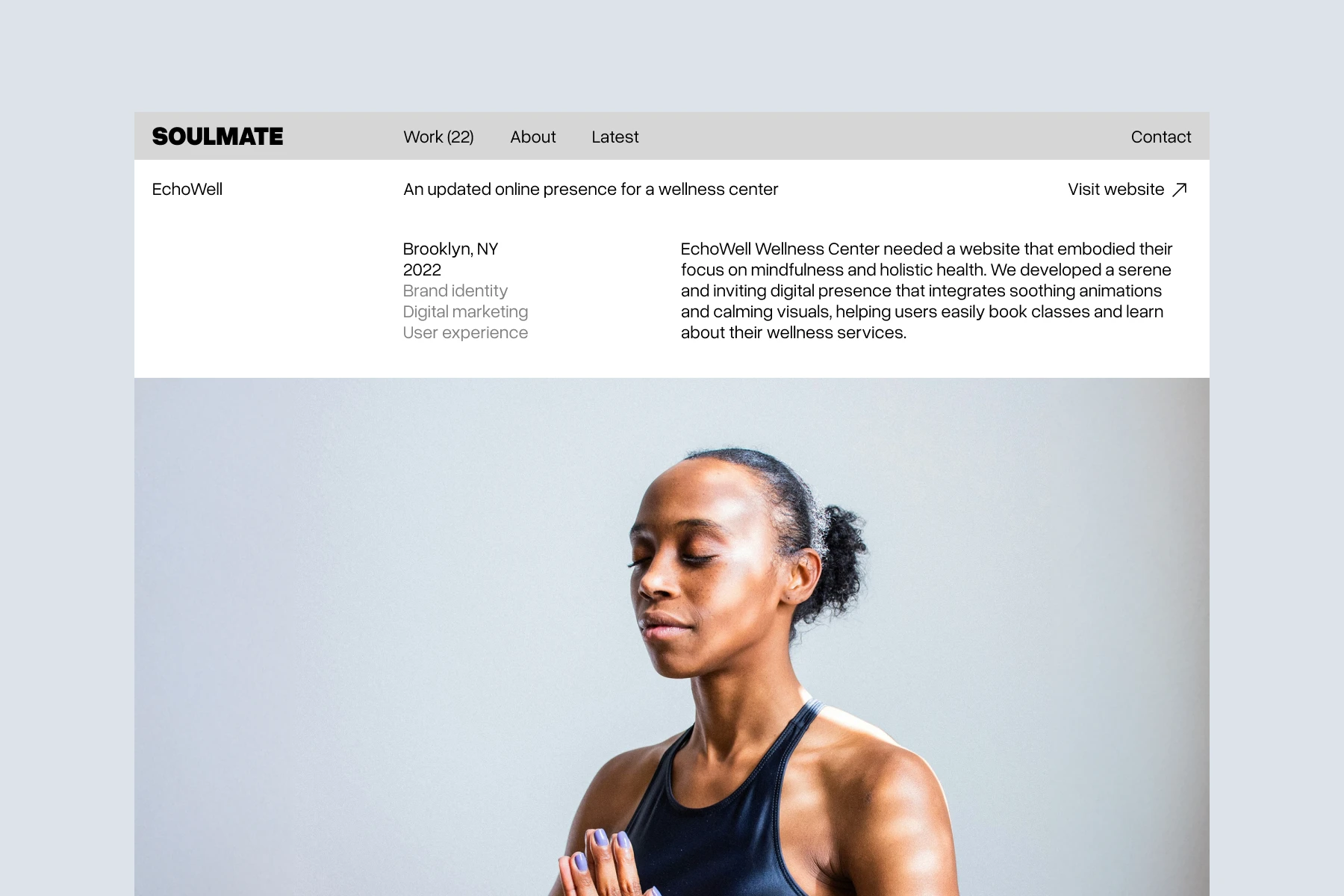 Serene young woman with eyes closed and hands in prayer pose, wearing a black tank top against a light background.