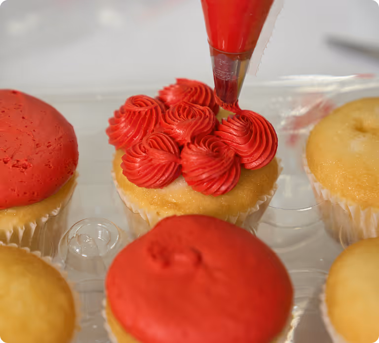 A cupcake being iced with red icing