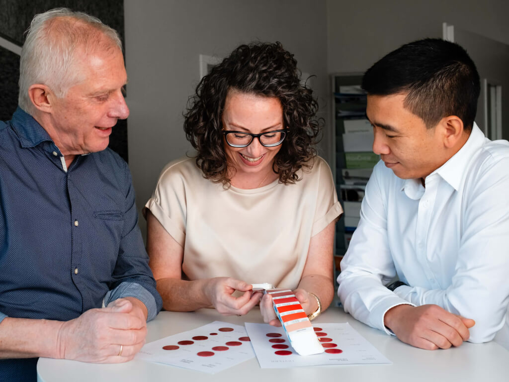 Drei Personen, die an einem Tisch sitzen und Farbmuster sowie Diagramme betrachten.