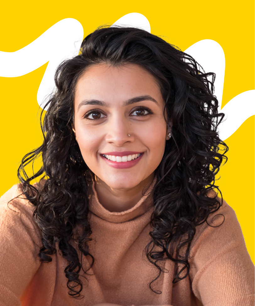 Smiling woman with curly dark hair wearing a light brown sweater against a yellow background with white abstract shapes.