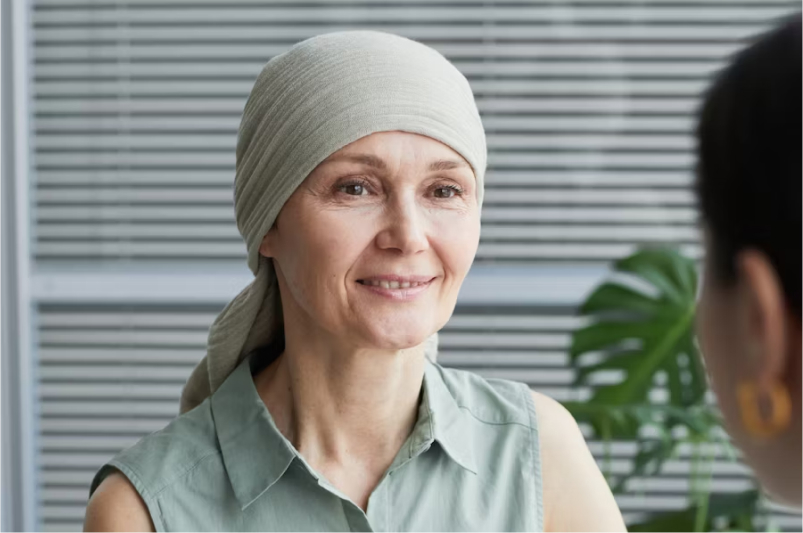 Smiling middle-aged woman wearing a headscarf and sleeveless shirt talking to another person indoors.