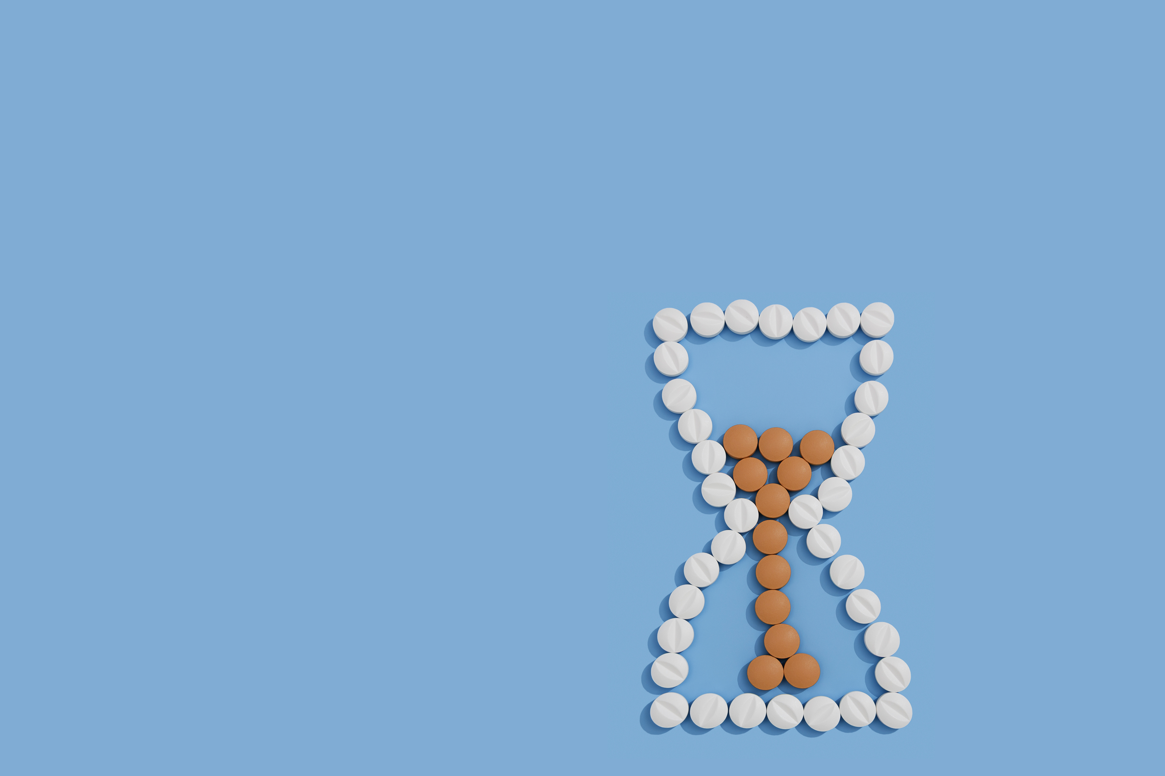 Hourglass shape made from white and brown round pills on a blue background.