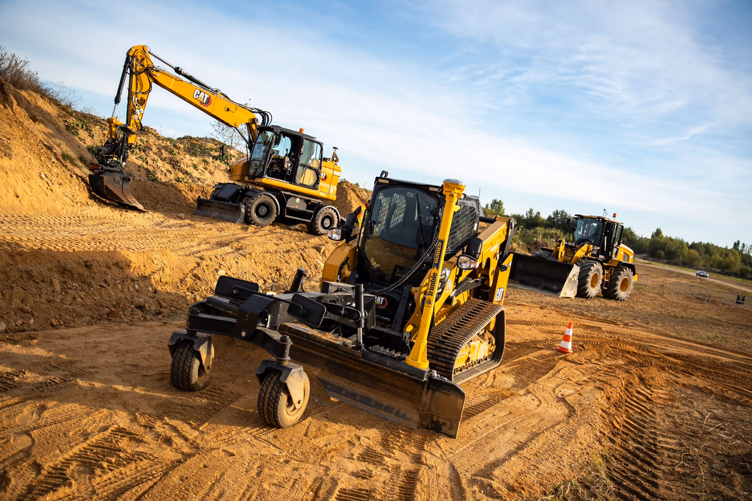 Žlutý nakladač CAT na staveništi s modrou oblohou a obláčky.